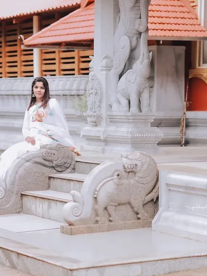 A wide shot showcasing the serene beauty of a temple entrance. The bride, dressed in white, sits peacefully on the steps, creating a tranquil and spiritual image.