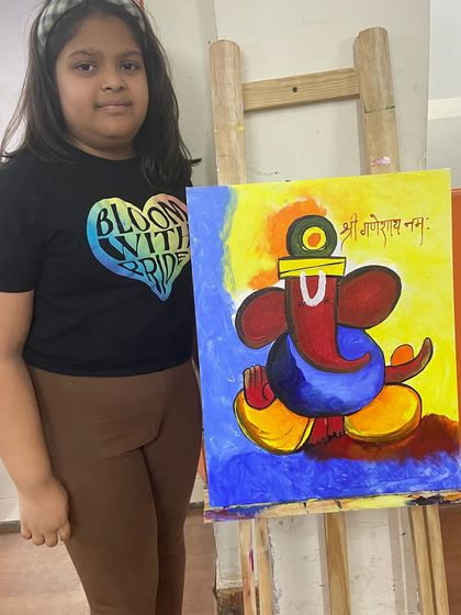 A student proudly stands by her vibrant, modern Ganesha painting on an easel. Our classes encourage students to explore different artistic styles, from traditional to contemporary.