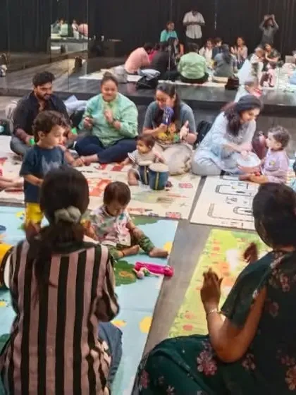 Our classes are a community circle where every family participates. You can see parents and children all engaged in a group music-making activity, which is the foundation of our sessions.