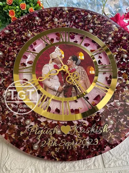 A large 16-inch clock featuring preserved pink and red rose petals from a wedding varmala. A central photo is framed by a golden dial, with the couple's names and date at the bottom.