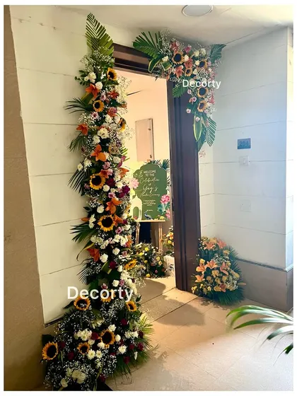 The entrance to a home decorated for a traditional ceremony, with a beautiful floral archway framing the door.