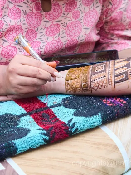 A behind-the-scenes shot of the mehndi artist at work, carefully drawing a design on the bride's arm. This photo documents the process and artistry that goes into your bridal henna.