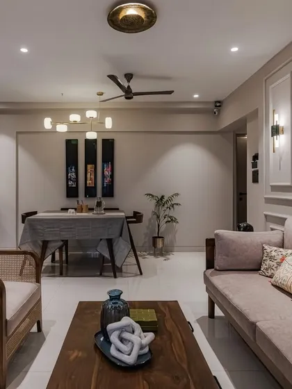 A different perspective of the same living and dining area, showing how the open-plan layout flows seamlessly. The consistent use of wood, rattan, and a neutral color scheme connects the spaces, while distinct lighting fixtures define the dining and lounging zones.
