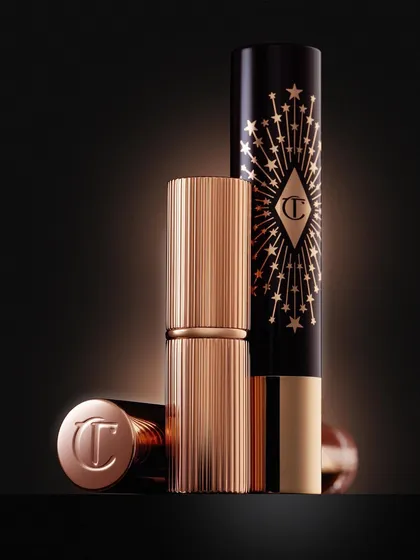 The texture and luxury of Charlotte Tilbury lipsticks are iconic. This shot focuses on the ribbed gold casing and the deep black packaging with its starburst design. The lighting is designed to make the gold gleam and feel incredibly premium.
