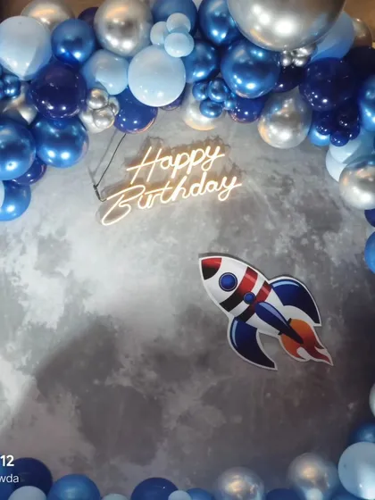It's all in the details. This close-up of an outer space theme shows a custom moon backdrop, a rocket cutout, and a modern neon 'Happy Birthday' sign, all framed by a deep blue and silver organic balloon garland. These little touches make a big impact.