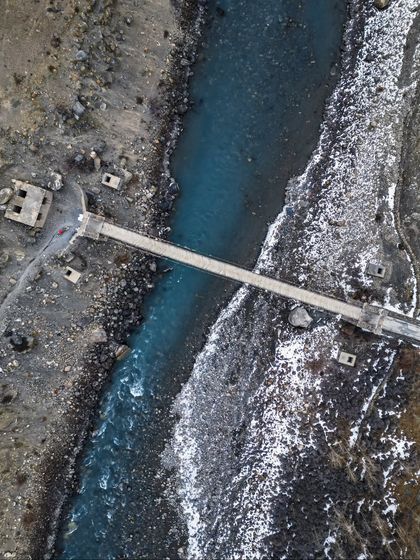A top-down drone view of a bridge crossing a glacial river in Spiti, highlighting the textures of the landscape.