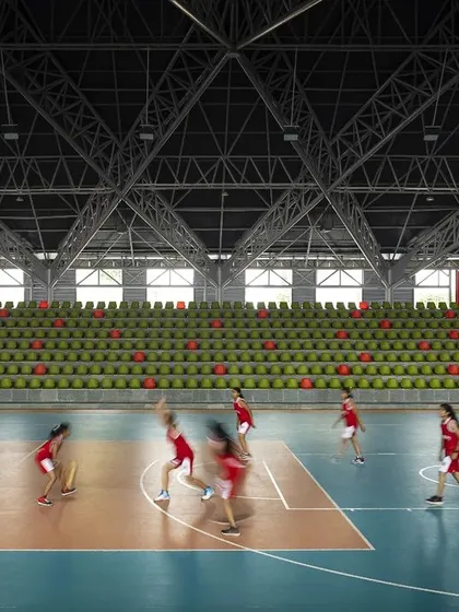 The 'Figured Ground' university sports arena captured in action, showcasing the expansive, column-free interior enabled by a complex truss roof system. The design accommodates large-scale activities like basketball while maintaining a visual connection to the tiered seating, creating an energetic and inclusive environment for athletes and spectators.