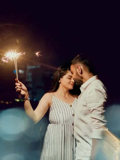 A couple shares an intimate moment at night, illuminated by the soft glow of a sparkler. The beautiful bokeh in the foreground adds a dreamy, magical quality to this pre-wedding photo.