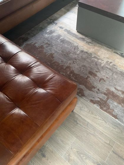 The rich texture of a tufted leather ottoman against a wooden floor and a subtly patterned rug.