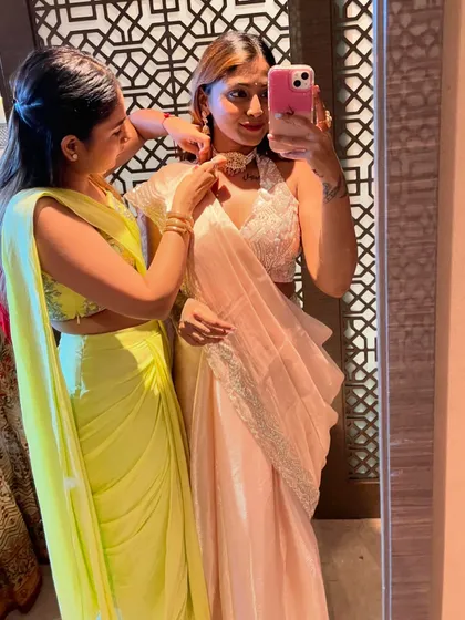 A friend helping me with the final touches on my jewelry. This moment captures the joy of getting ready for an Indian wedding, wearing a beautiful light pink saree with an embellished blouse.