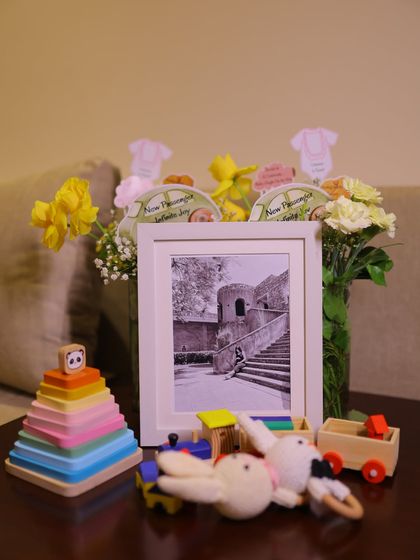 A beautifully styled tabletop with personal touches. A framed photo of the parents-to-be is surrounded by fresh flowers, wooden toys, and handmade rattles, reflecting a natural and elegant theme.