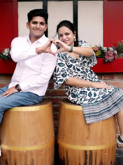 A cute and casual shot with a European cafe theme, complete with barrels for seating and an "Underground" sign. The couple forms a heart with their hands, adding a sweet touch.