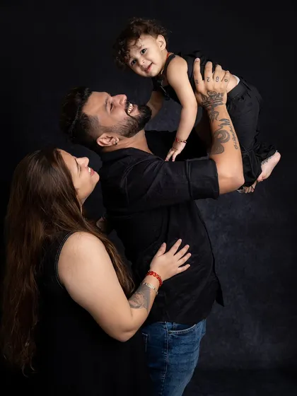 A beautiful family portrait against a dark backdrop. The parents are looking lovingly at their child, creating a powerful and emotional image.