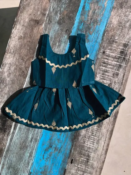 Our handloom cotton dress in a rich teal shade, adorned with delicate gold detailing and a playful pleated skirt. The scalloped edges and comfy fabric make it perfect for festive adventures.