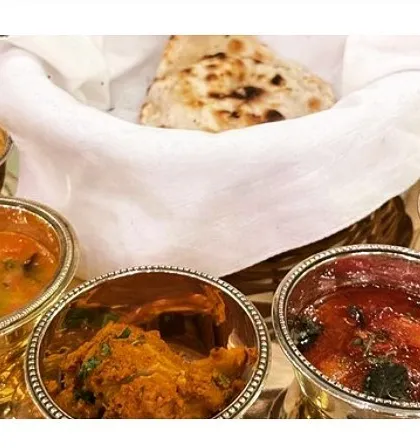 A traditional Indian thali setup with various curries served in elegant silver bowls alongside a basket of fresh naan.