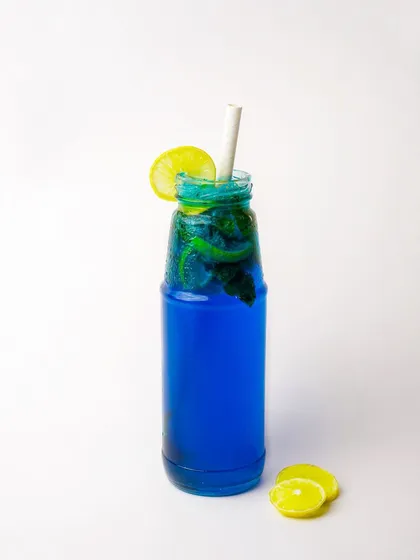 A striking blue curaçao mojito in a bottle, garnished with lemon and mint.