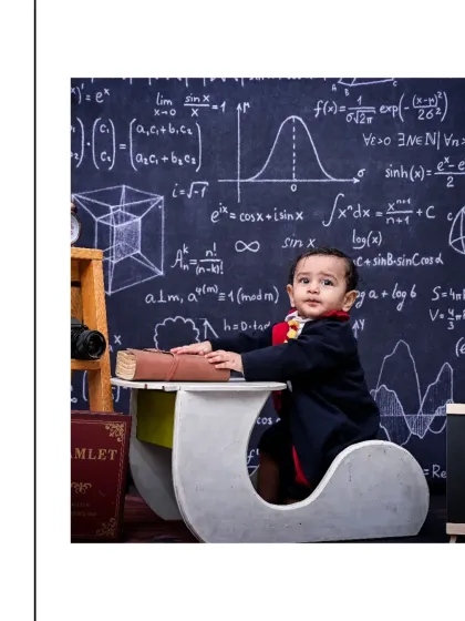 A thoughtful portrait of a baby dressed in a wizard robe, sitting at a desk with a large book. The chalkboard background filled with formulas adds a whimsical, academic feel to this creative shoot.