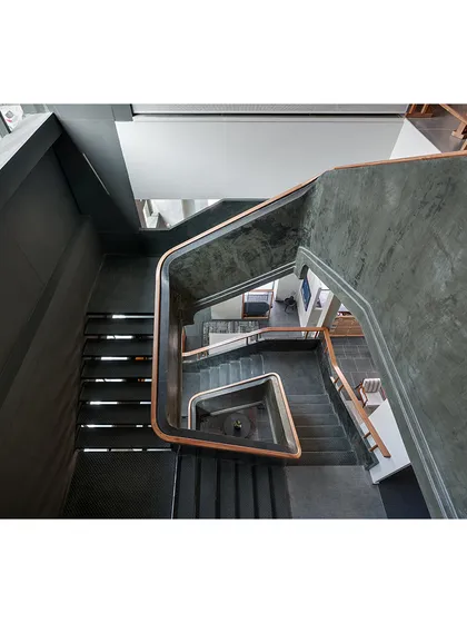 The main staircase at the Magari store is a sculptural element, with a sweeping ferrocement railing and wooden handrail that guides visitors through the multi-level showroom.