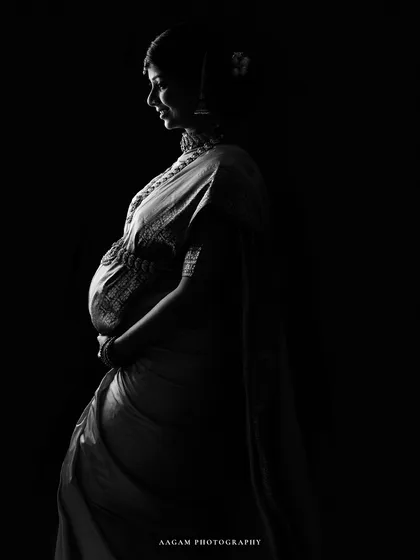 A breathtaking silhouette of a mother-to-be in a traditional saree. The light catches the beautiful details of the fabric and her jewelry, celebrating her heritage.