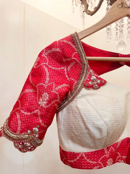 A classic combination of a crimson red and off-white saree blouse, embellished with zardosi embroidery, designed for a gold-tone Mysore silk saree.