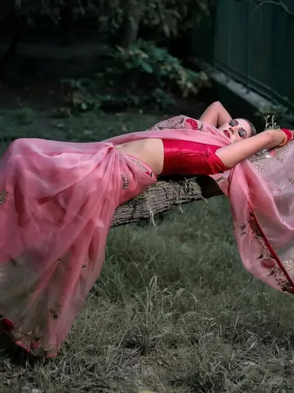 An artistic, high-fashion pose with the model lying on a tree branch, the pink saree draping beautifully.