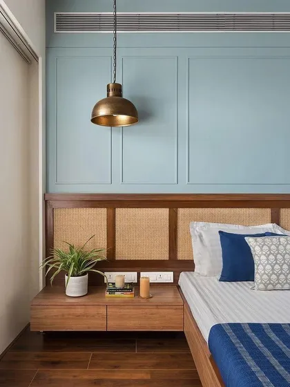 A modern take on classic materials. This bedroom features a beautiful cane-paneled headboard set against a calming blue accent wall with decorative molding, blending traditional texture with contemporary color.