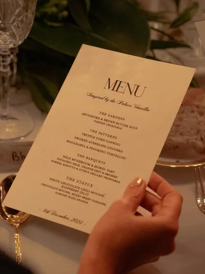 A guest holding a beautifully designed menu for a dinner inspired by the Palace of Versailles. The menu itself is an important part of the storytelling and overall guest experience.