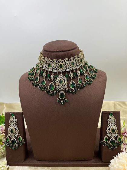 An elegant AD zircon and green stone choker set, perfect for a reception or sangeet ceremony. The intricate silver-toned metalwork is paired with deep green hanging beads.