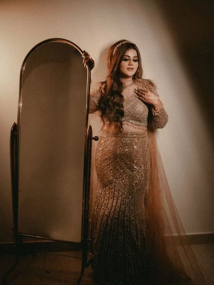 A full-length portrait of the bride standing next to a mirror. Her elegant pose and the classic setting highlight her sophisticated bridal style.