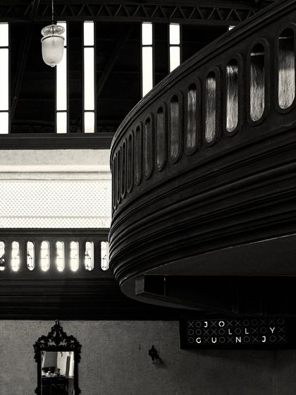 A composition showing the layers of the space: the mezzanine balcony, a vintage mirror below, and the tall windows in the background.