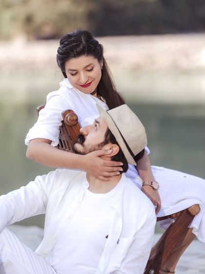 A tender moment on the beach, with her sitting on a vintage chair and caressing his face. This is a beautifully composed, intimate portrait.