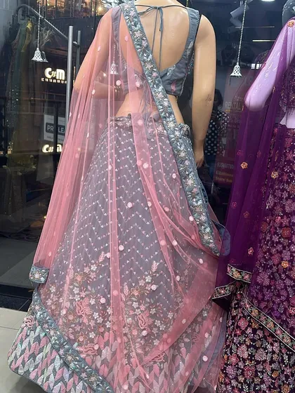 A back view of a grey lehenga with pink and blue floral embroidery on a mannequin, showing the intricate details and back design of the blouse.