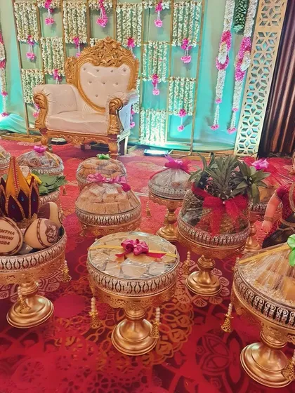 A wide view of a Seemantha platter arrangement on a vibrant red carpet. We filled ornate platters with traditional sweets, dry fruits, decorated coconuts, and even a decorated pineapple to add to the festive display.