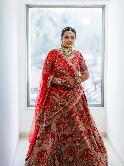 A full-length shot of the bride by a window, creating a beautiful, naturally lit portrait. Her smile radiates happiness, and her makeup looks fresh and flawless.