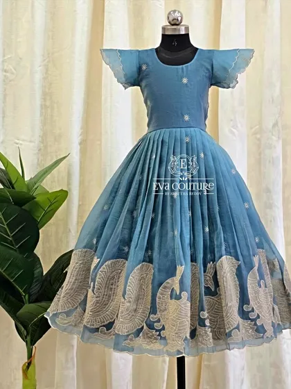 A light blue frock with delicate silver peacock embroidery along the border. The flutter sleeves add a soft, modern touch.