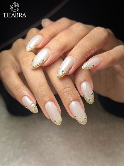 A full hand view of the pearl-finished nude extensions with gold chrome borders and rhinestone accents.