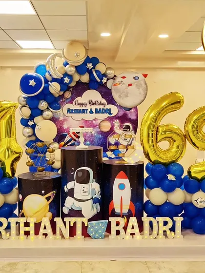 A space-themed party for a 4th and 69th birthday. The decor includes astronaut and rocket cutouts, planet-themed plinths, and large foil number balloons.