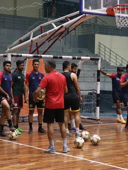 A coach instructs his futsal team during a training session on our wooden court. The basketball hoop in the background shows the multi-sport adaptability of our arena.