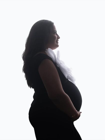 A classic high-key silhouette. The clean white background creates a stark and beautiful outline, focusing completely on the mom-to-be and her baby bump.