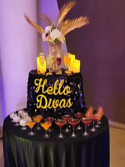A 'Hello Divas' welcome drink station for a ladies' night out. The sequined table and floral arrangement add a touch of glamour to the event.
