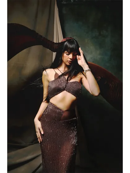 A portrait focusing on the texture of the sequined Ambika Lal outfit. The wind-blown hair and thoughtful pose add a sense of life and movement to the studio shot.