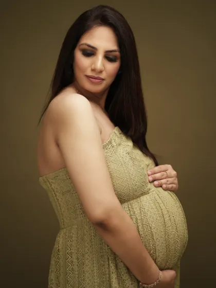 A simple and beautiful close-up portrait. The expecting mother in a lovely green lace dress cradles her bump, creating a classic and elegant maternity photo.
