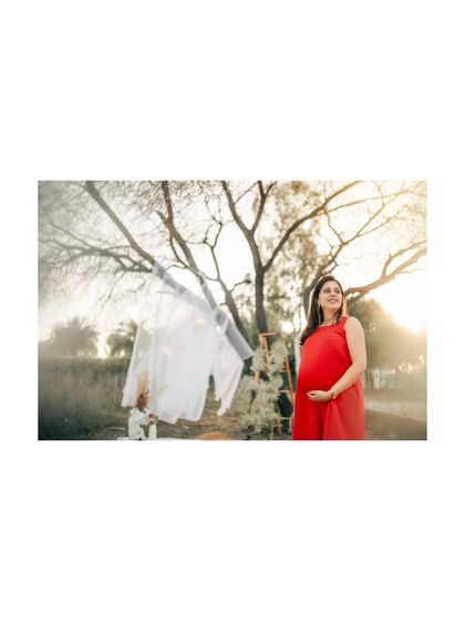 A wider view of the outdoor scene, with the mom-to-be in her red dress. The setup with a clothesline and white fabric adds a whimsical and rustic touch to the shoot.