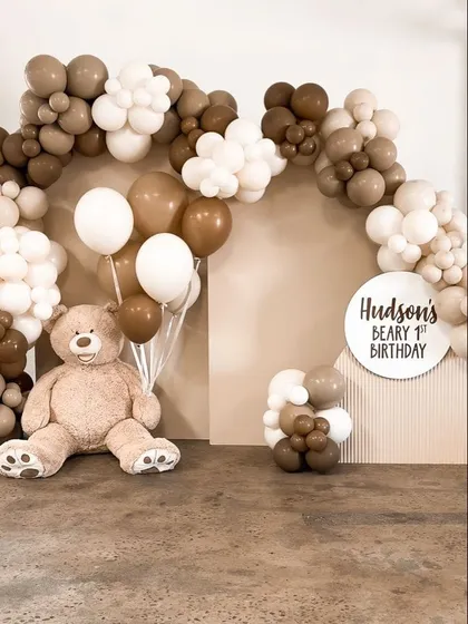 A minimalist and modern teddy bear first birthday theme. This "Hudson's Beary 1st Birthday" setup uses a neutral palette of brown and white balloons with a large teddy bear.