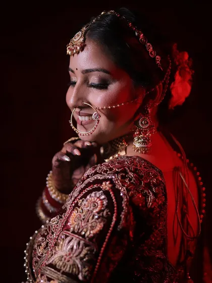 A smiling bridal portrait, with the bride looking back over her shoulder, against a rich, red-lit background.
