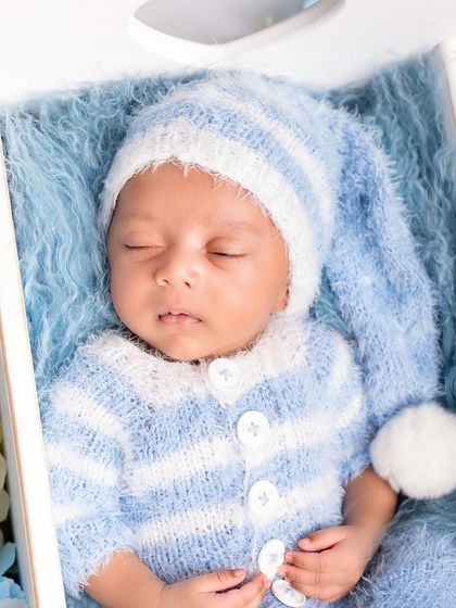 A handsome little boy in a blue and white striped knit outfit, sleeping in a white wooden crate surrounded by blue hydrangeas.