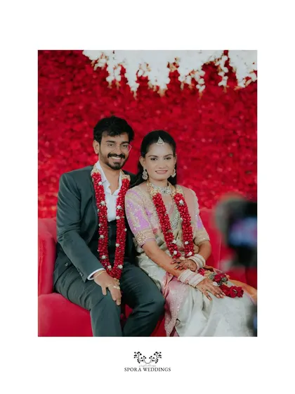 The couple seated for a portrait against a stunning wall of red flowers, a vibrant and romantic backdrop.