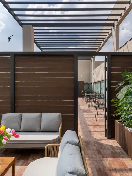 This seating area on the terrace, complete with a comfortable sofa and modern pergola, provides a sheltered space for team gatherings or quiet breaks. The design uses natural wood tones to create a warm, inviting atmosphere.