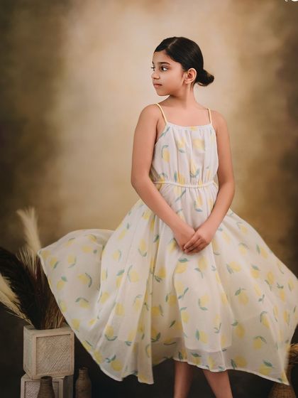 A graceful, full-length portrait of a young girl in a lemon-print dress, looking elegant and poised.
