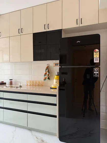 A detail shot focusing on the high-gloss black refrigerator and how it integrates with the cream and black cabinetry, creating a seamless and modern look.